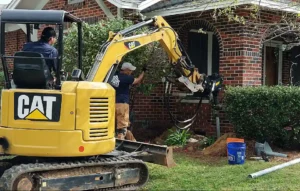 MDH Foundation Repair technician using a mini excavator to install helical piers in a gulf coast home